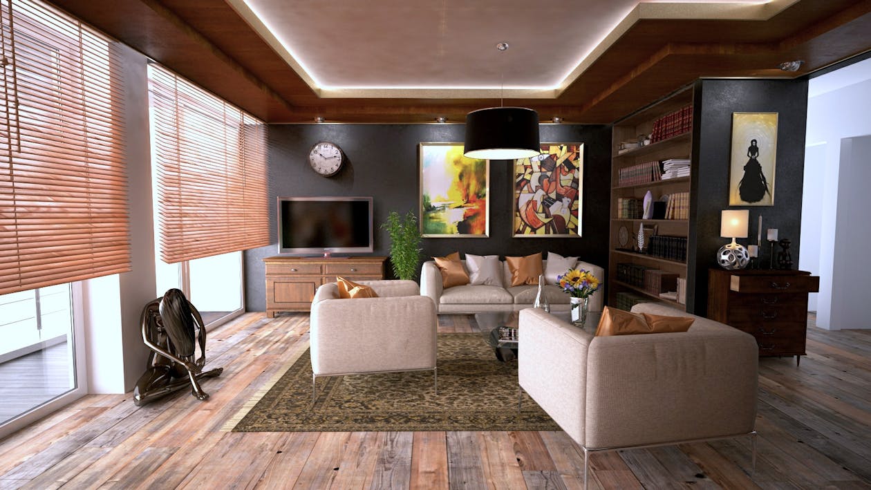 A set of modern house keys lies on a wooden table in the foreground, with the sunlit, beautifully designed interior of a luxury home softly blurred in the background.