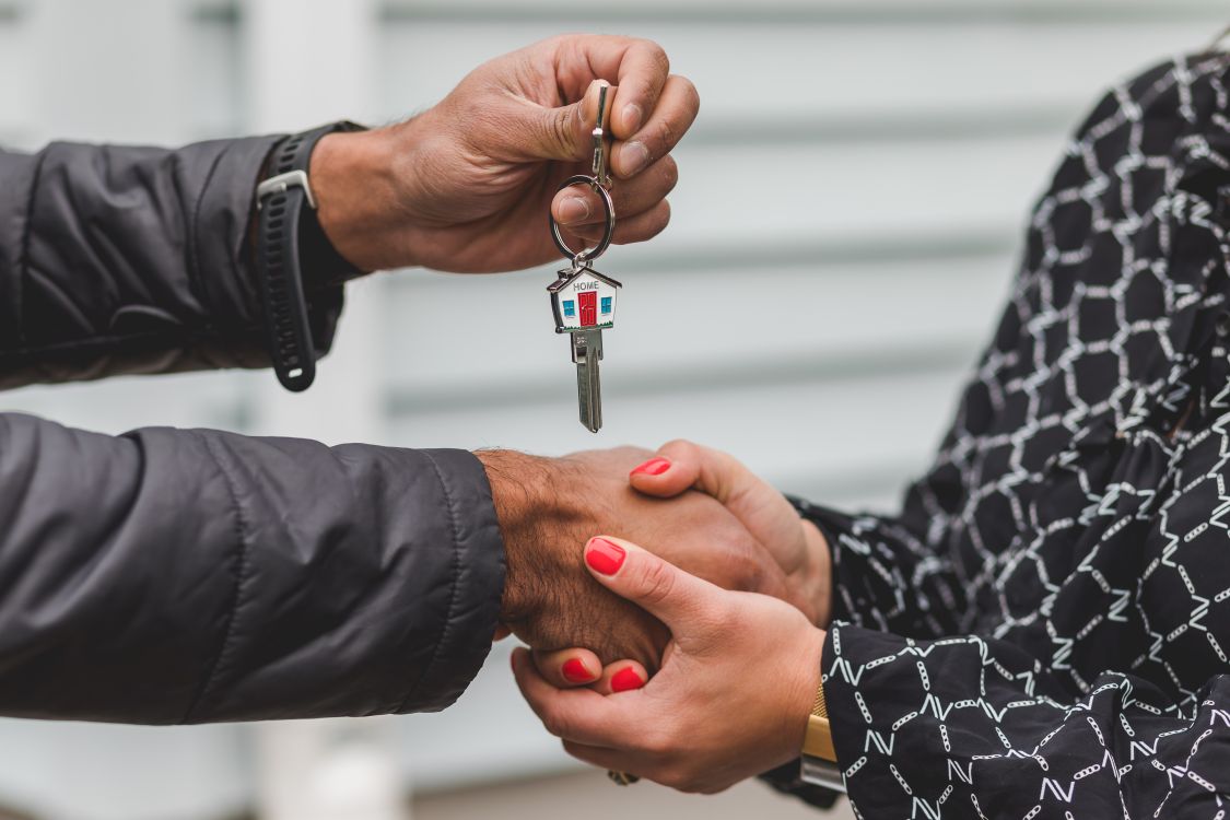 A happy couple shakes hands with a professional real estate agent across a kitchen island in a bright, modern home, signifying a successful sale.