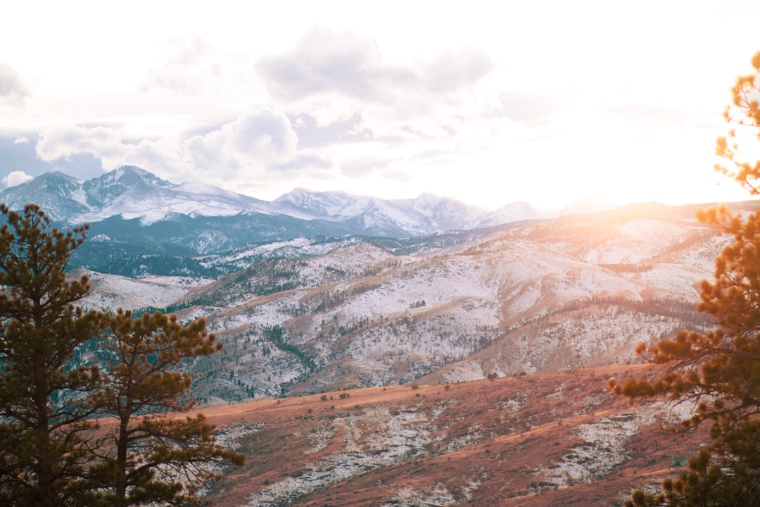 Lone hiker stands on a rocky outcrop at sunrise, looking out at the majestic Pikes Peak in Colorado, symbolizing ambition ...