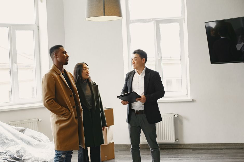 A professional real estate agent sits with a couple at a modern table, attentively listening and discussing options, highlighting the personal negotiation and advocacy Zillow lacks.