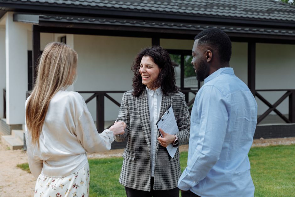 A real estate agent smiles while handing over house keys to an excited couple, representing the successful outcome of a client-centric model.